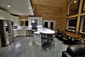 A modern kitchen with stainless steel appliances, a central island, and a dining area with leather seating.