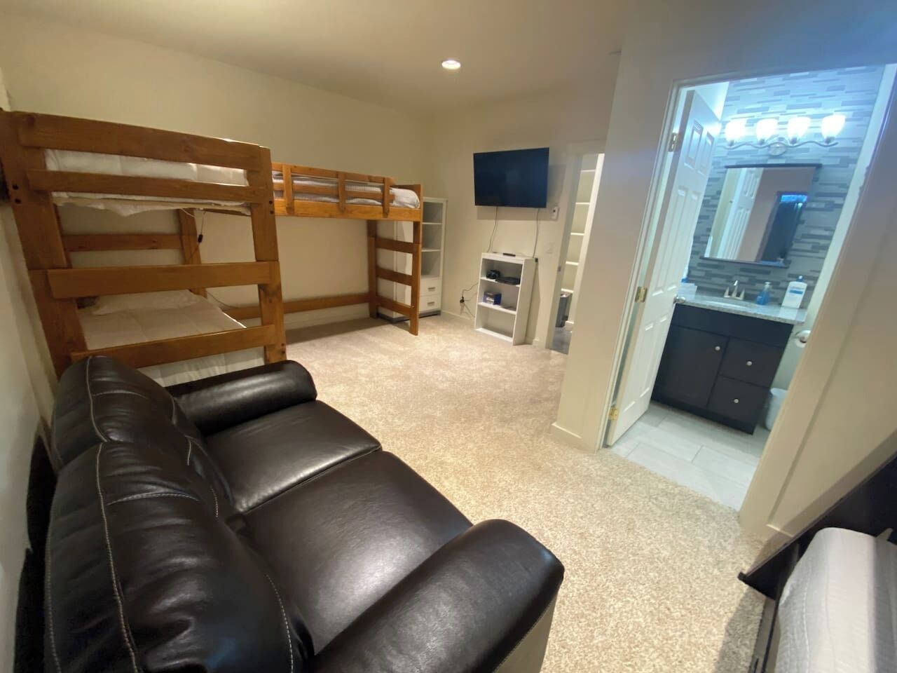 Quarto com beliche, sofá de couro, televisão e área de cozinha.