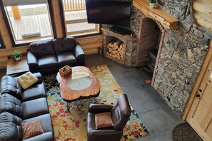Un salon chaleureux avec une cheminée en pierre, des canapés en cuir et un téléviseur à écran plat.