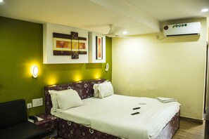 A hotel room with a bed, a bedside table with a phone, a wall-mounted air conditioner, and two framed artworks on the wall. - Hotel Platinum (Kolkata)