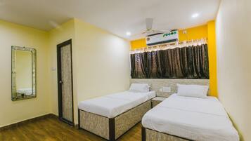 Habitación de hotel con dos camas individuales, ventilador de techo, equipo de aire acondicionado y un espejo en la pared.