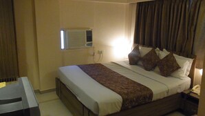 A hotel room with a bed, a bedside table, a lamp, and an air conditioning unit. - Hotel Eden (Ahmedabad)
