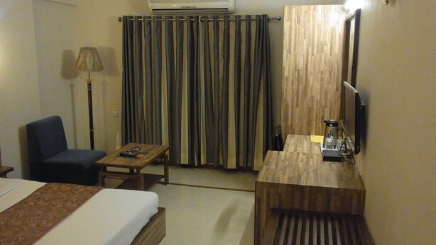 A hotel room with a bed, a desk, a chair, a lamp, a TV, and a wooden panel wall. - Hotel Eden (Ahmedabad)
