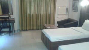 A hotel room with two beds, a desk, a chair, a small table, and a curtain. - Hotel Eden (Ahmedabad)