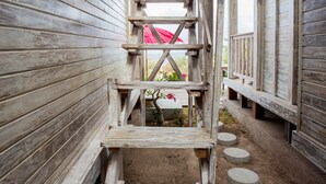 Eine Holztreppe führt zu einem überdachten Bereich, im Hintergrund ist ein roter Sonnenschirm zu sehen.