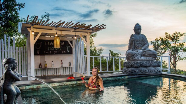 Ein Poolbereich mit einer Buddha-Statue, einer hölzernen Konstruktion mit einem Schild und einer Person im Wasser.