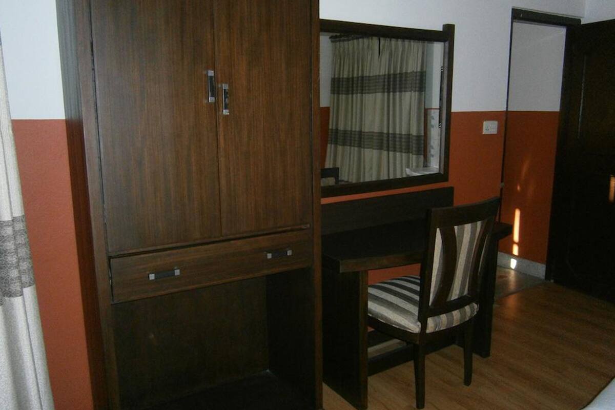 A room with a wooden wardrobe, a mirror, a striped chair, and a bed with a striped blanket.