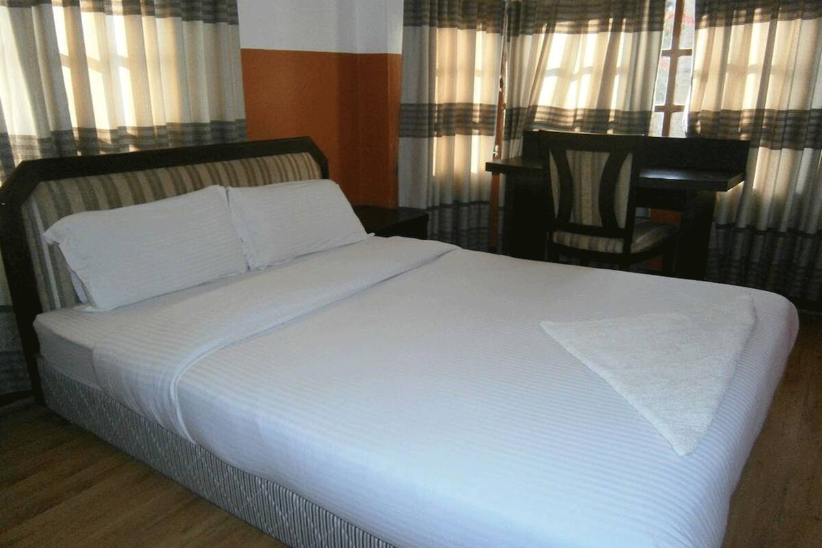 A neatly made bed with white linens, a wooden headboard, and a small table with a chair beside it.