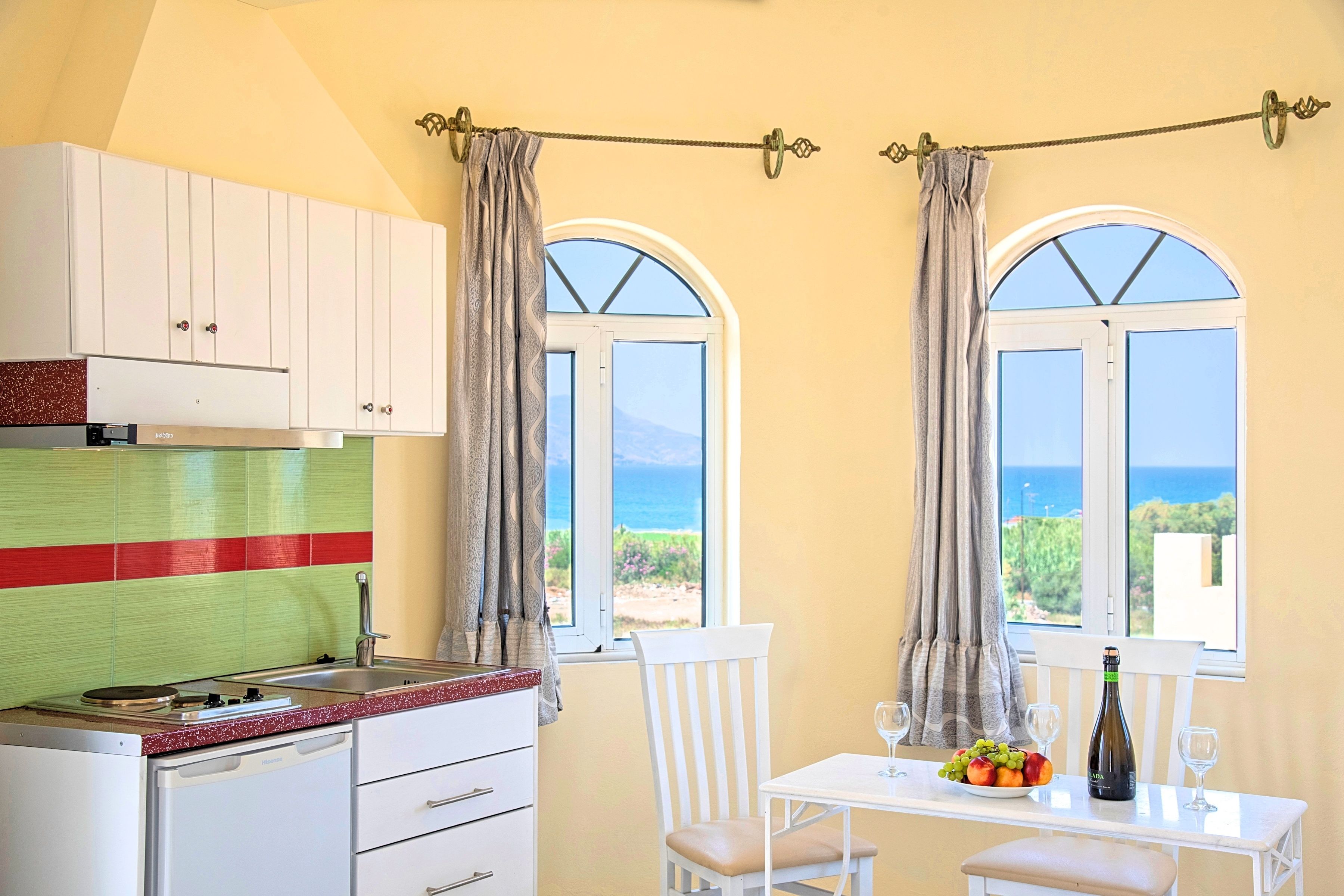 Una cocina con vista al mar, una mesa de comedor con una botella y vasos, y una silla.