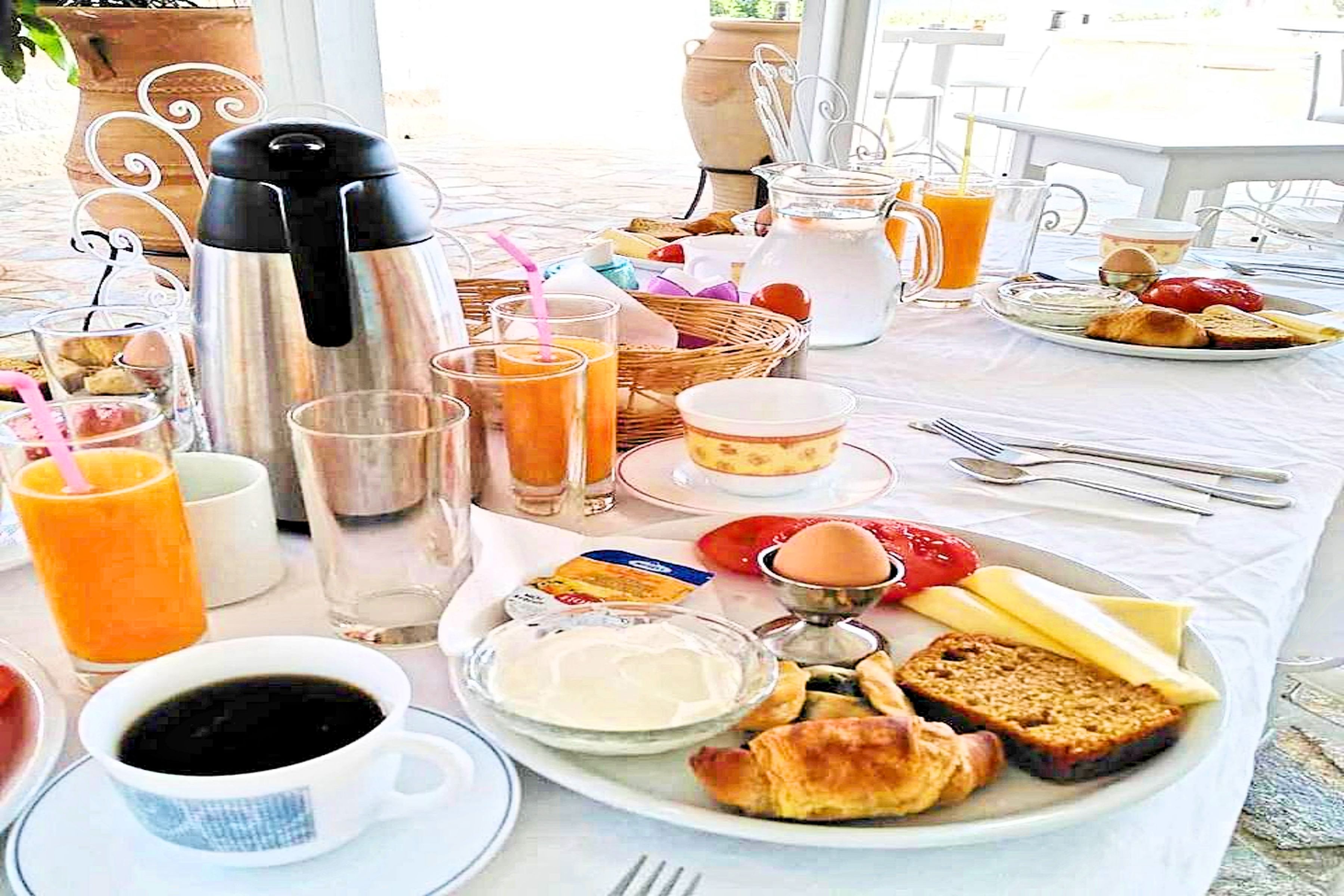 A breakfast table with a coffee pot, orange juice, eggs, toast, and a basket of bread.
