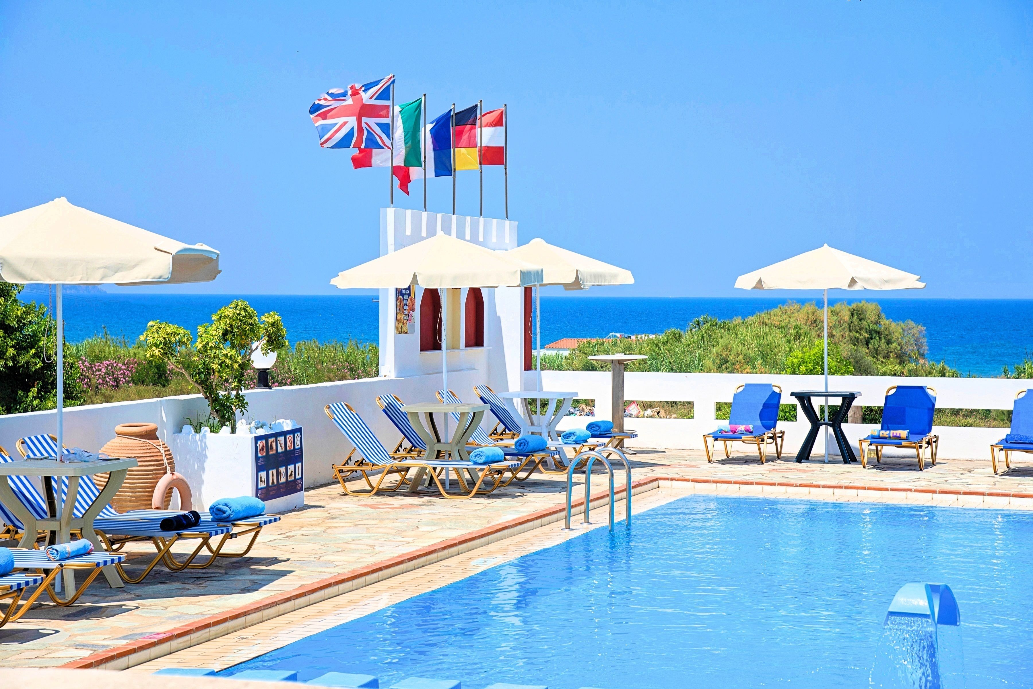 A poolside area with lounge chairs, umbrellas, and flags.