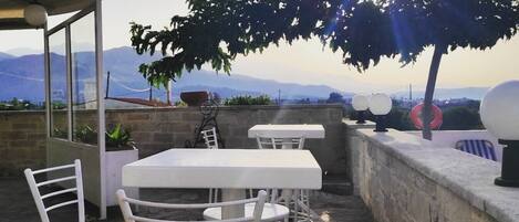 An outdoor patio with a table and chairs, a stone wall, and a view of mountains.