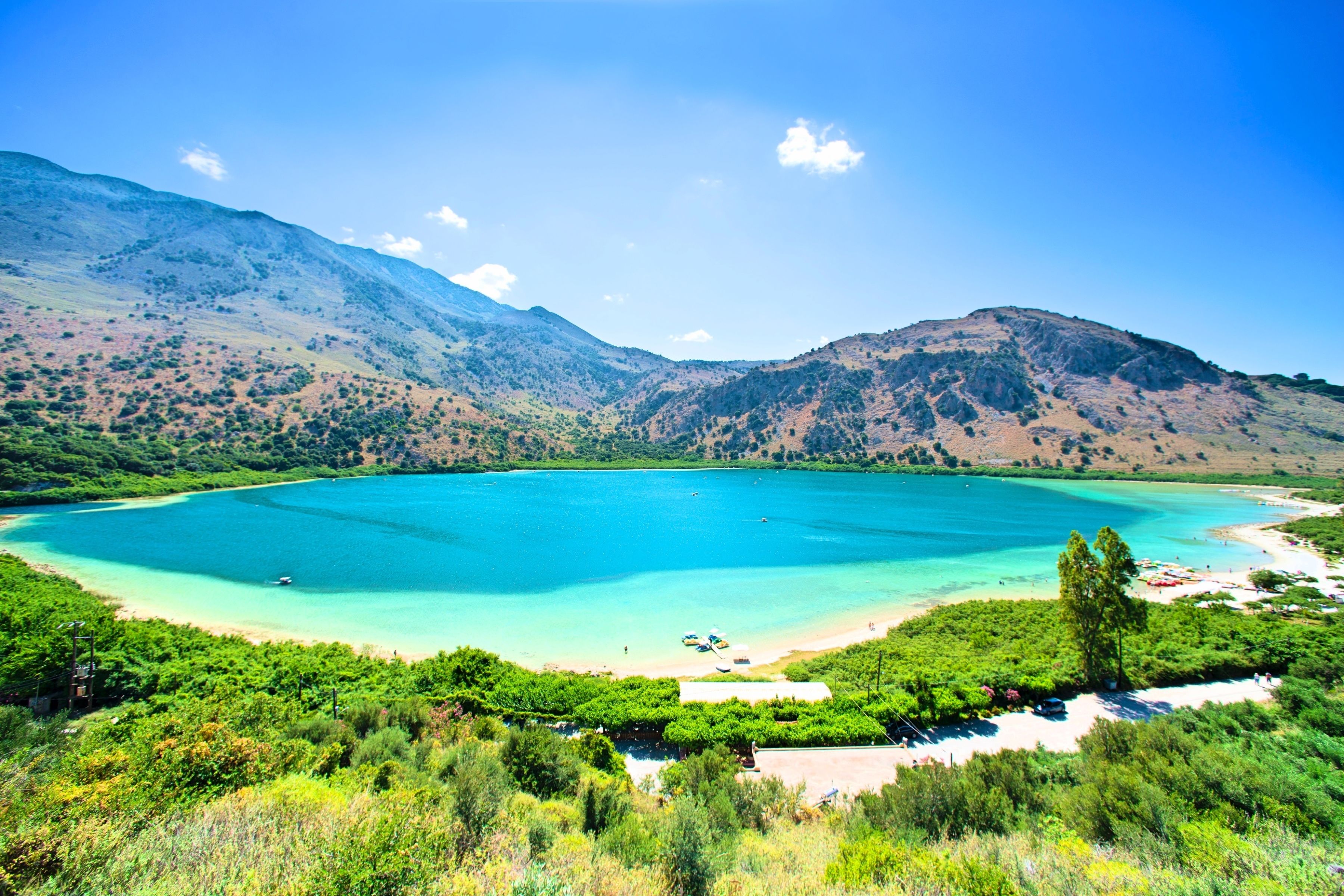 Eine Küstenlandschaft mit einem großen, türkisblauen See, umgeben von grünen Hügeln und wolkenlosem Himmel.