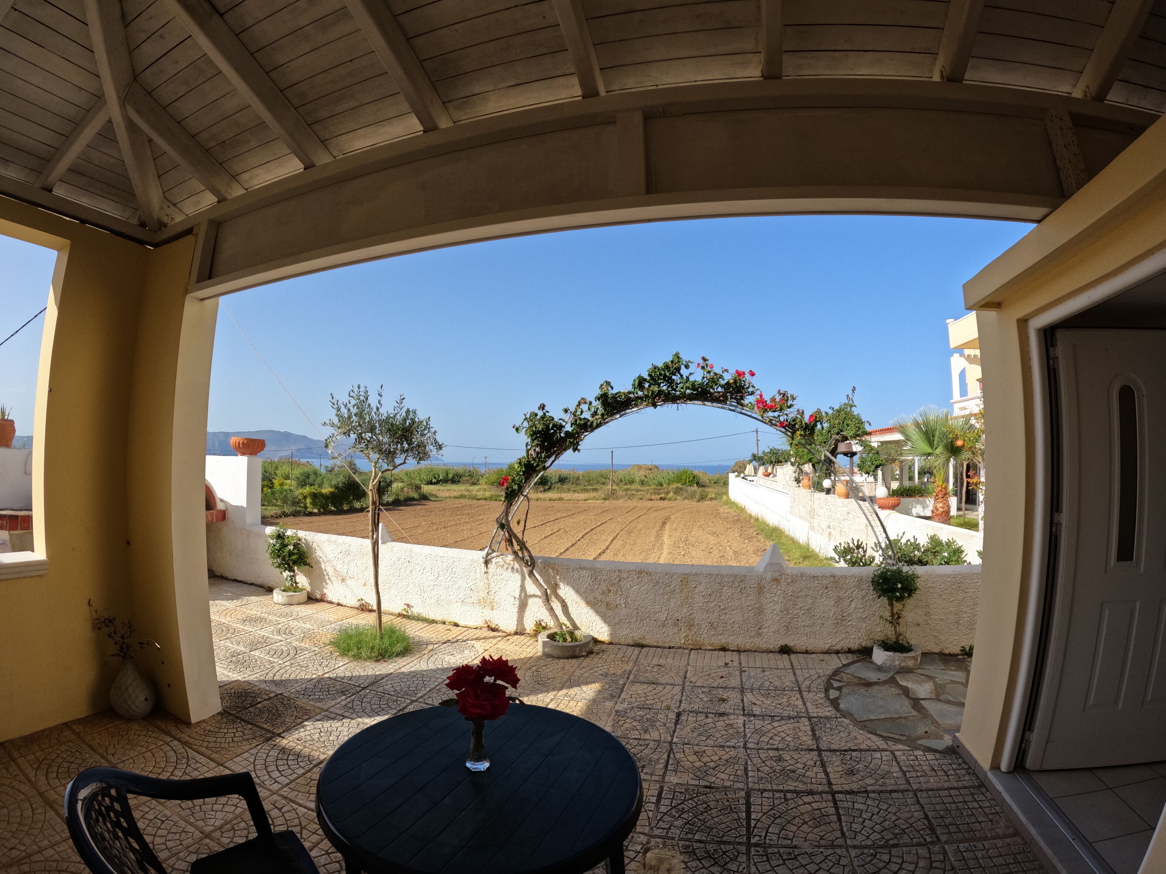 A covered patio with a table and chairs, a decorative archway, and a view of a landscaped area and distant mountains.