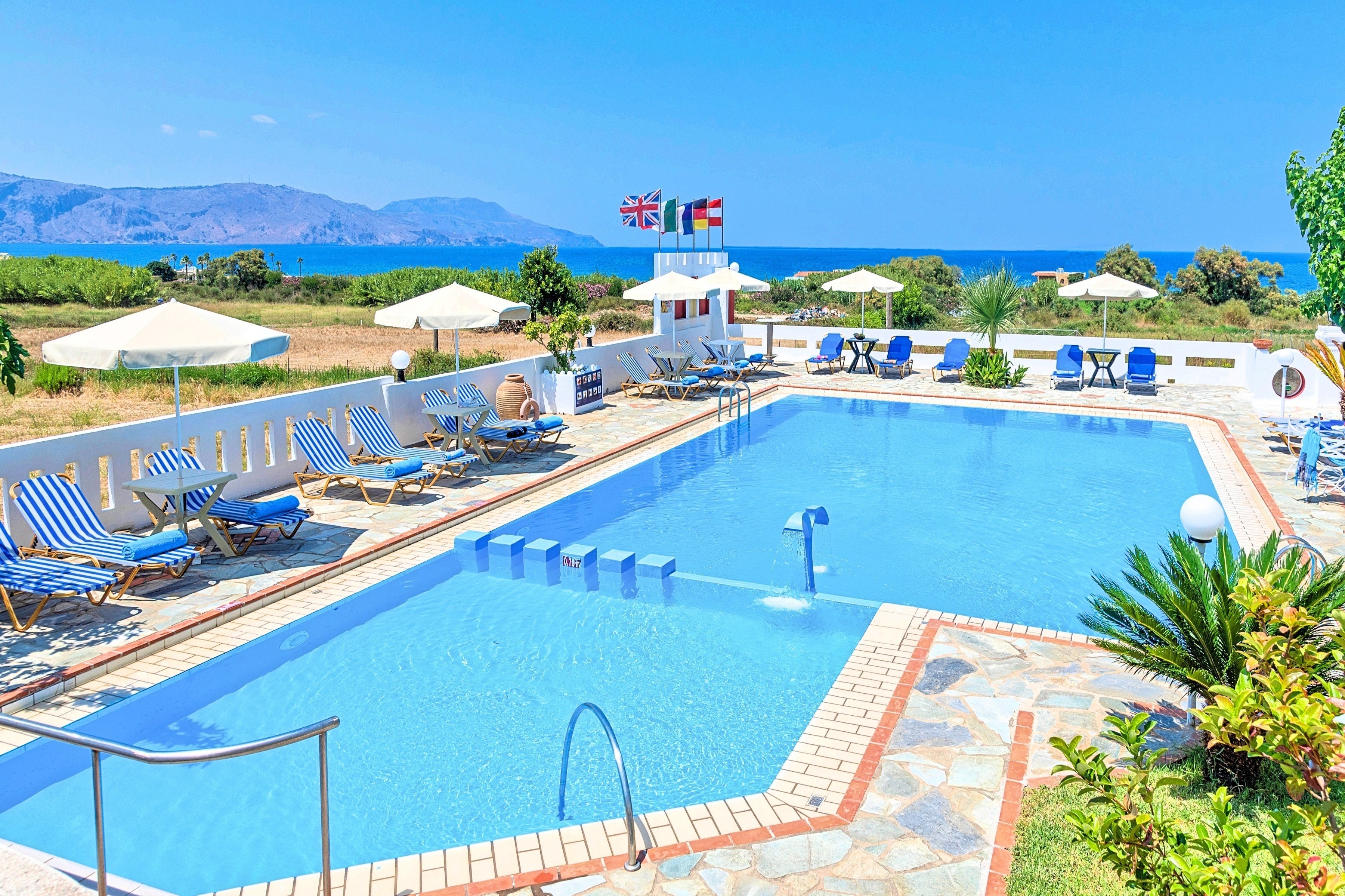 A swimming pool with lounge chairs and umbrellas, flags, and a view of the sea.