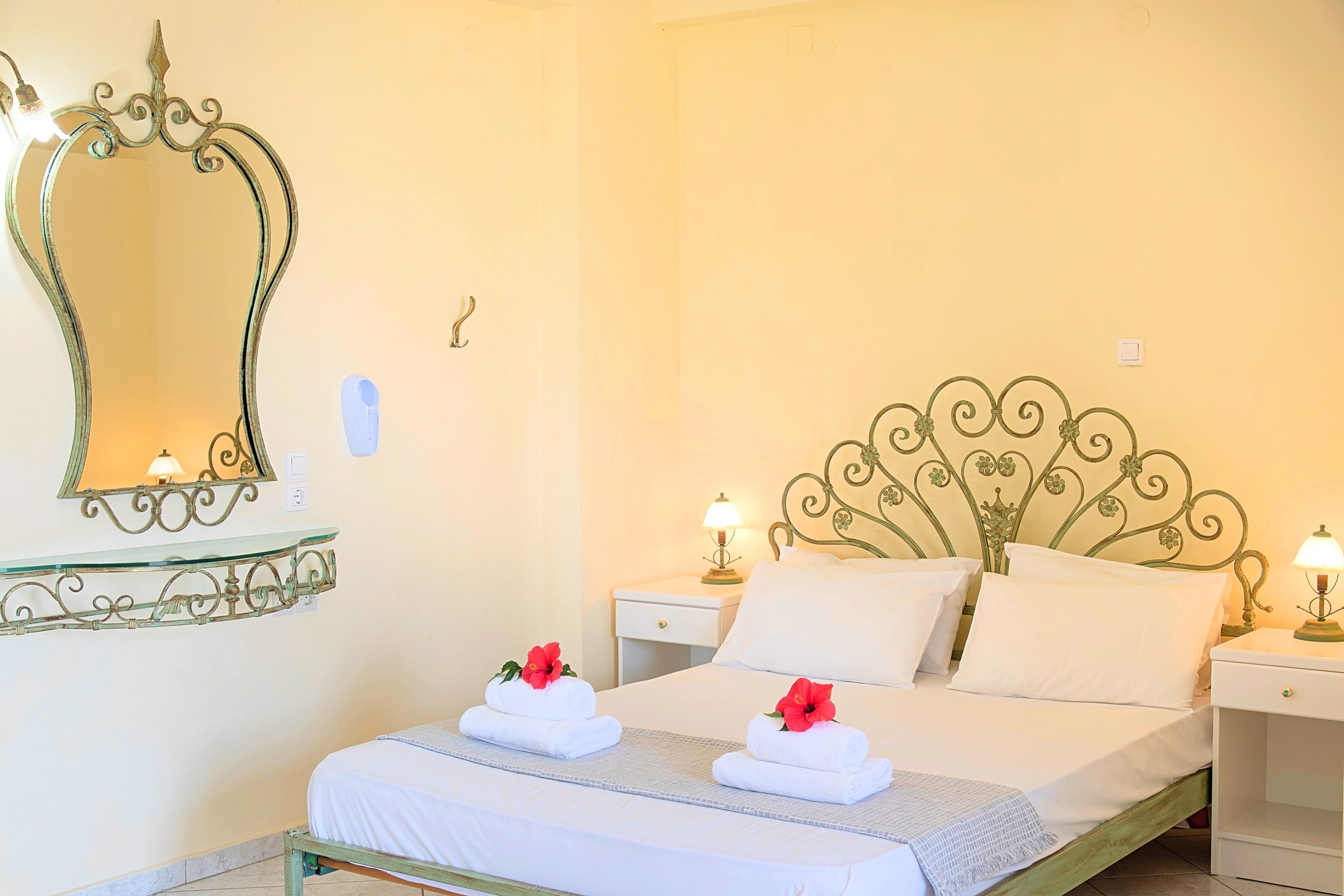 A hotel room with a bed, two bedside tables with lamps, a decorative mirror, and a wall-mounted light switch.