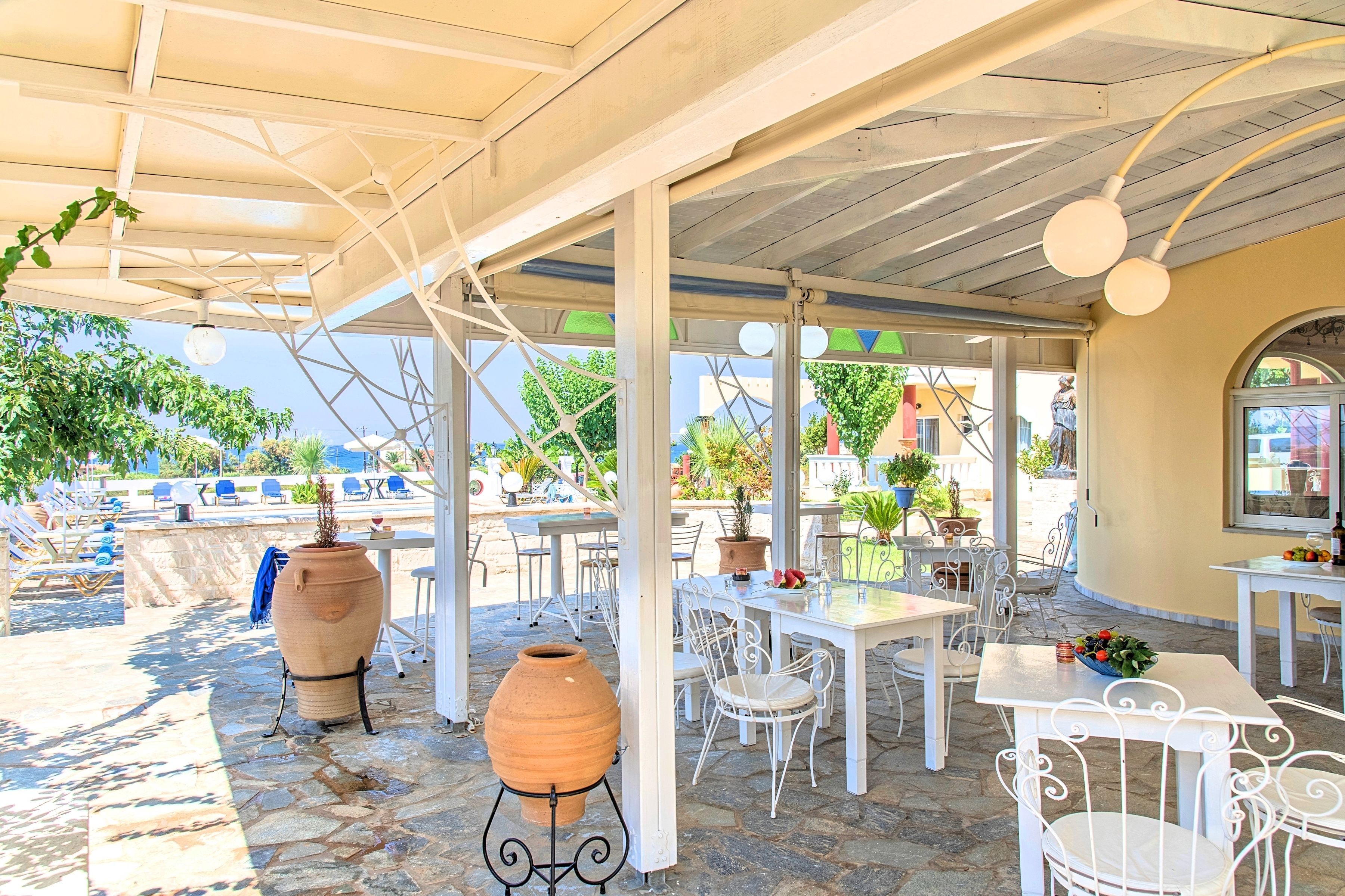 An outdoor patio area with stone flooring, white metal chairs, tables, and potted plants.