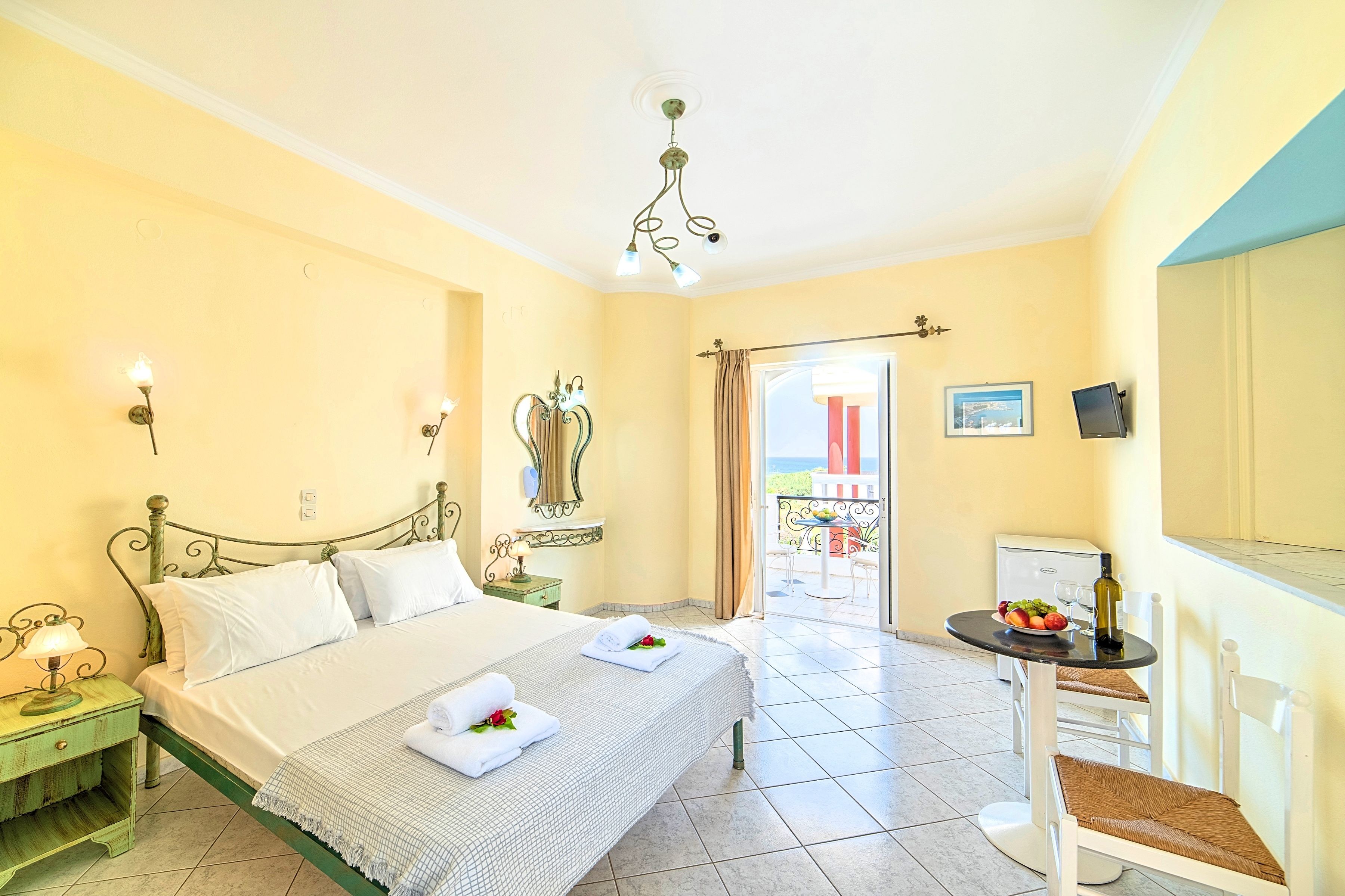 A hotel room with a bed, a small table with a chair, a balcony with a table and chairs, and a view of the outside.