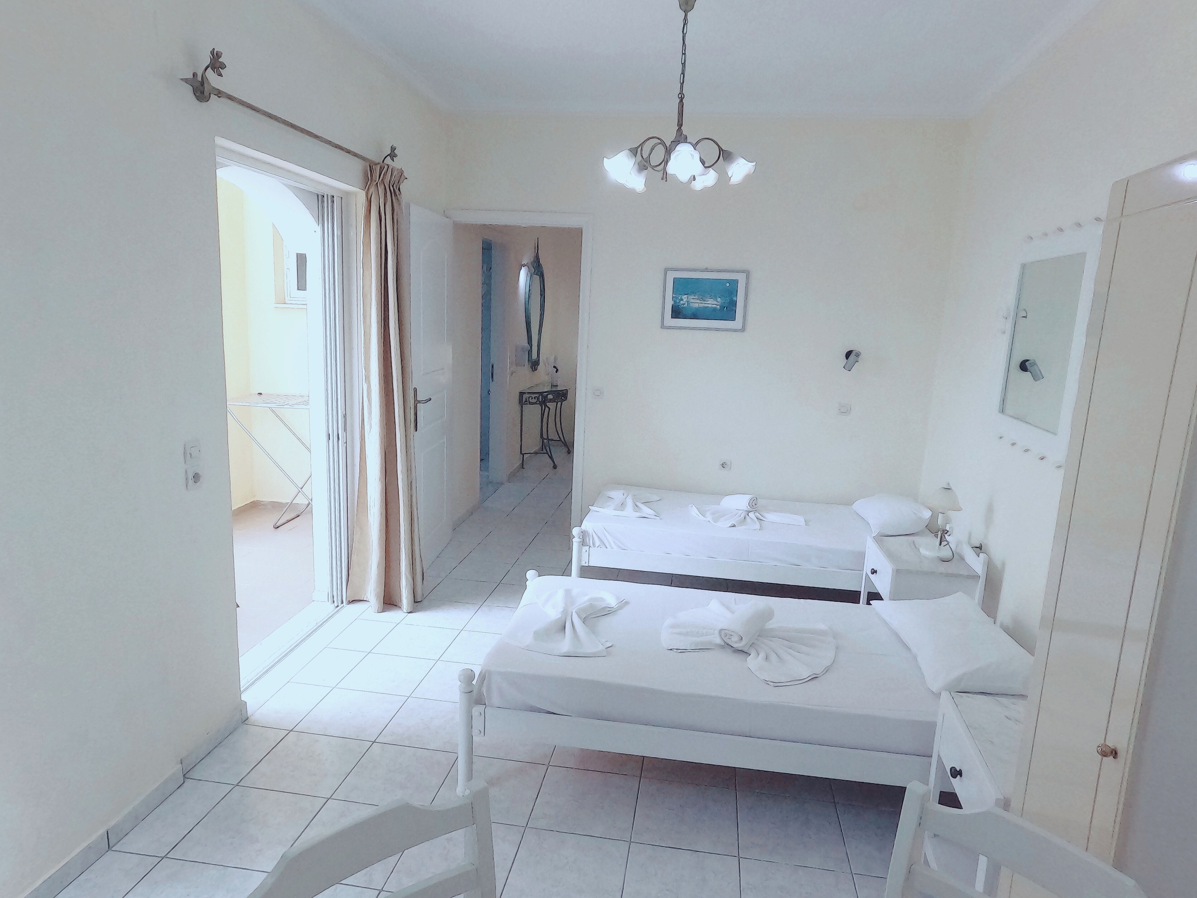 Une chambre d’hôtel avec deux lits, un lustre, un tableau et une porte dotée d’un miroir.