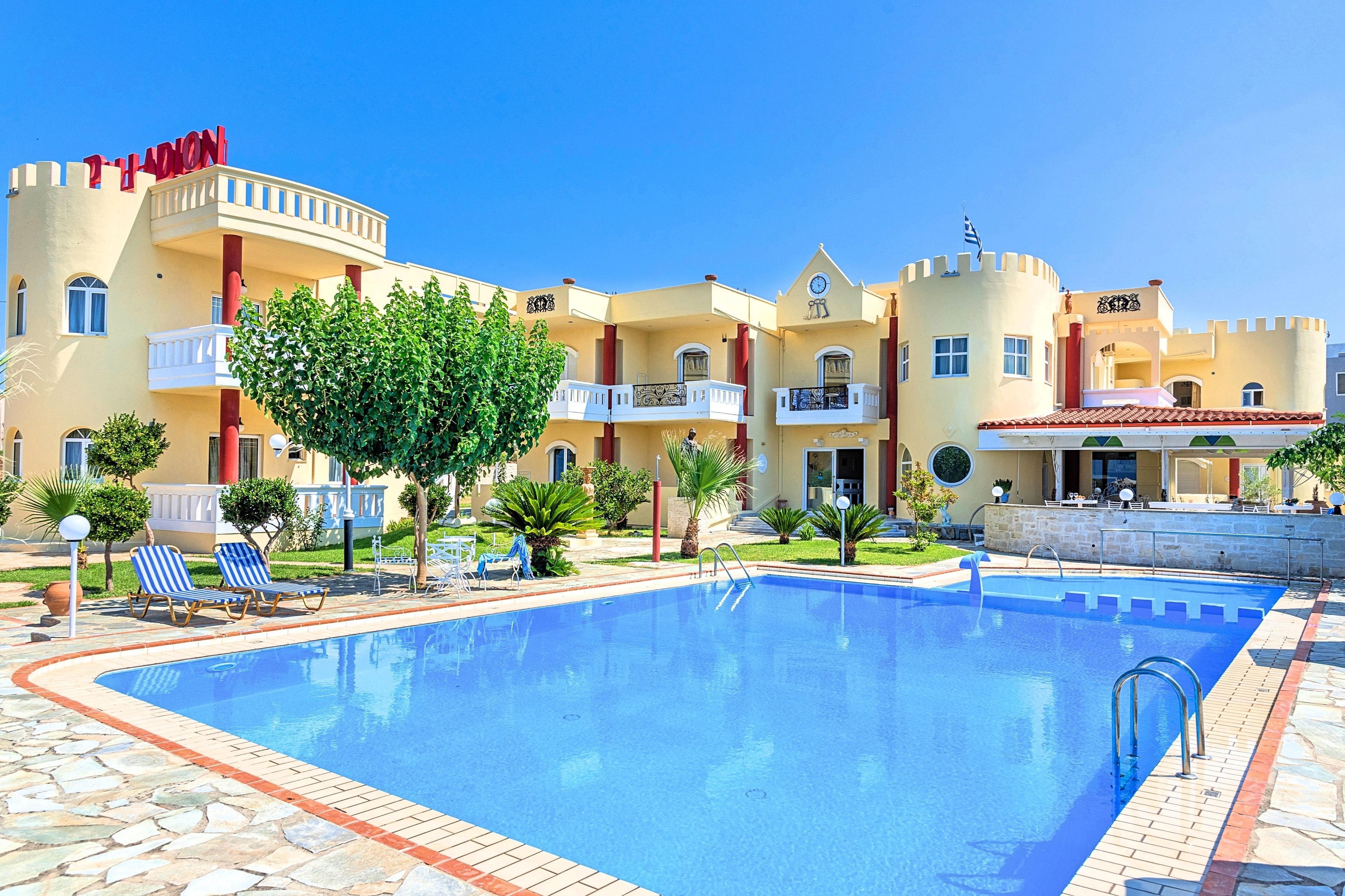 A hotel with a swimming pool, lounge chairs, and a castle-like facade.