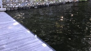 A wooden dock extending into a calm river, surrounded by lush greenery and a stone wall. - Lake Joseph 3 Bedroom Cottage and Bunkie (MacTier)