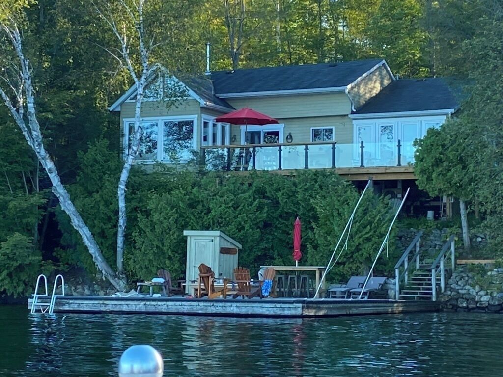 Ein Haus am Seeufer mit Steg, Sitzgelegenheiten im Freien und einem überdachten Bereich.