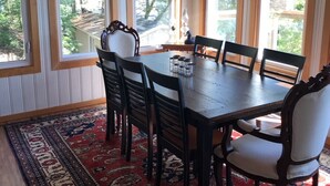 A dining area with a wooden table and chairs, large windows, and a patterned rug. - Lake Joseph 3 Bedroom Cottage and Bunkie (MacTier)