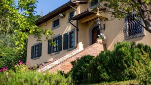 A two-story house with a brick staircase leading to the entrance, surrounded by lush greenery and flowering plants. - Villa with swimming pool, tennis court and table tennis ideal for sports lovers and the enjoyment of (Castiglion Fiorentino)