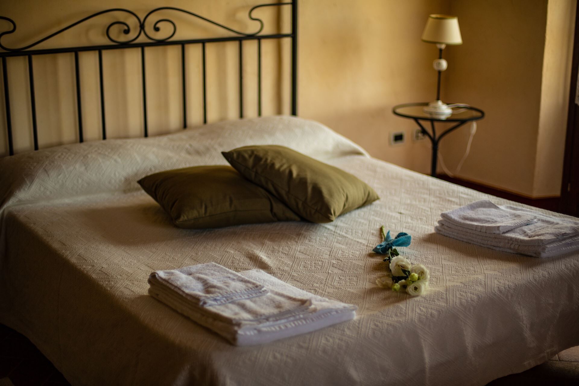 A neatly made bed with pillows, folded towels, and a small decorative item on a textured bedspread.