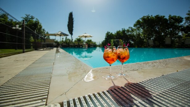 A poolside view with two drinks on a ledge, clear sky, and surrounding greenery. - Villa with swimming pool, tennis court and table tennis ideal for sports lovers and the enjoyment of (Castiglion Fiorentino)