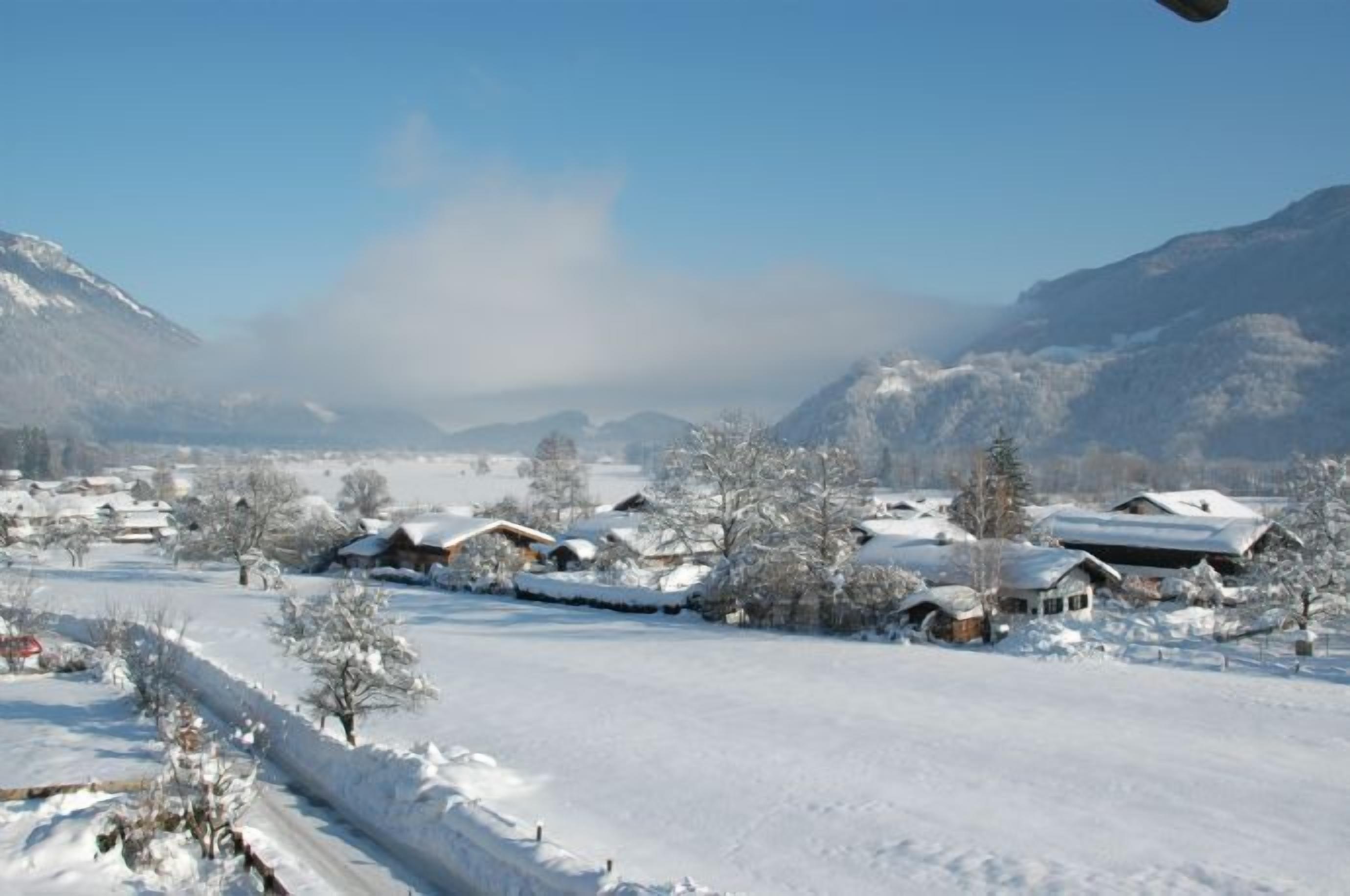 Uma aldeia coberta de neve, com casas e montanhas ao fundo.