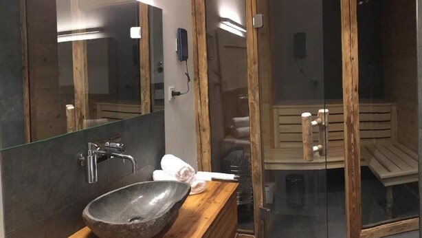 Un baño moderno con tocador de madera, lavabo de piedra y cabina de ducha de vidrio.