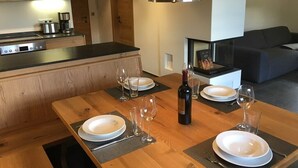Un comedor con una mesa de madera dispuesta para cuatro personas, una botella de vino y una cocina moderna al fondo.