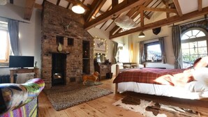A rustic room with exposed wooden beams, a stone fireplace, a bed with a red blanket, a television, and a dog. - Low Mill Guest House (Leyburn)