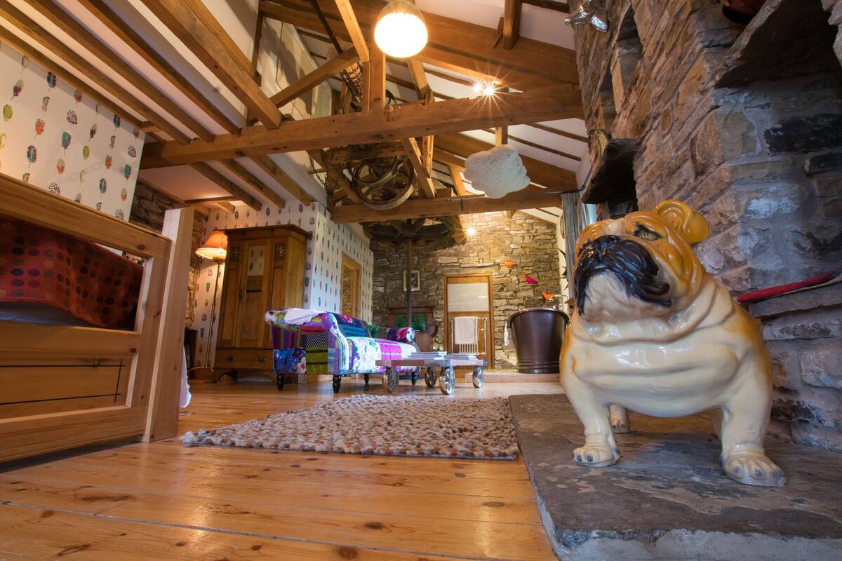 A rustic interior with exposed wooden beams, a stone fireplace, and a pug statue.
