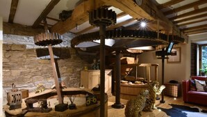 A rustic interior with exposed wooden beams, a stone wall, and a large wooden mill wheel. - Low Mill Guest House (Leyburn)