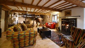 A rustic living room with exposed wooden beams, a fireplace, and a variety of seating including a patterned sofa and a red armchair. - Low Mill Guest House (Leyburn)
