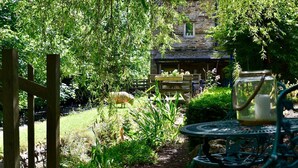 A garden with a wooden gate, a table with chairs, and a stone building in the background. - Low Mill Guest House (Leyburn)