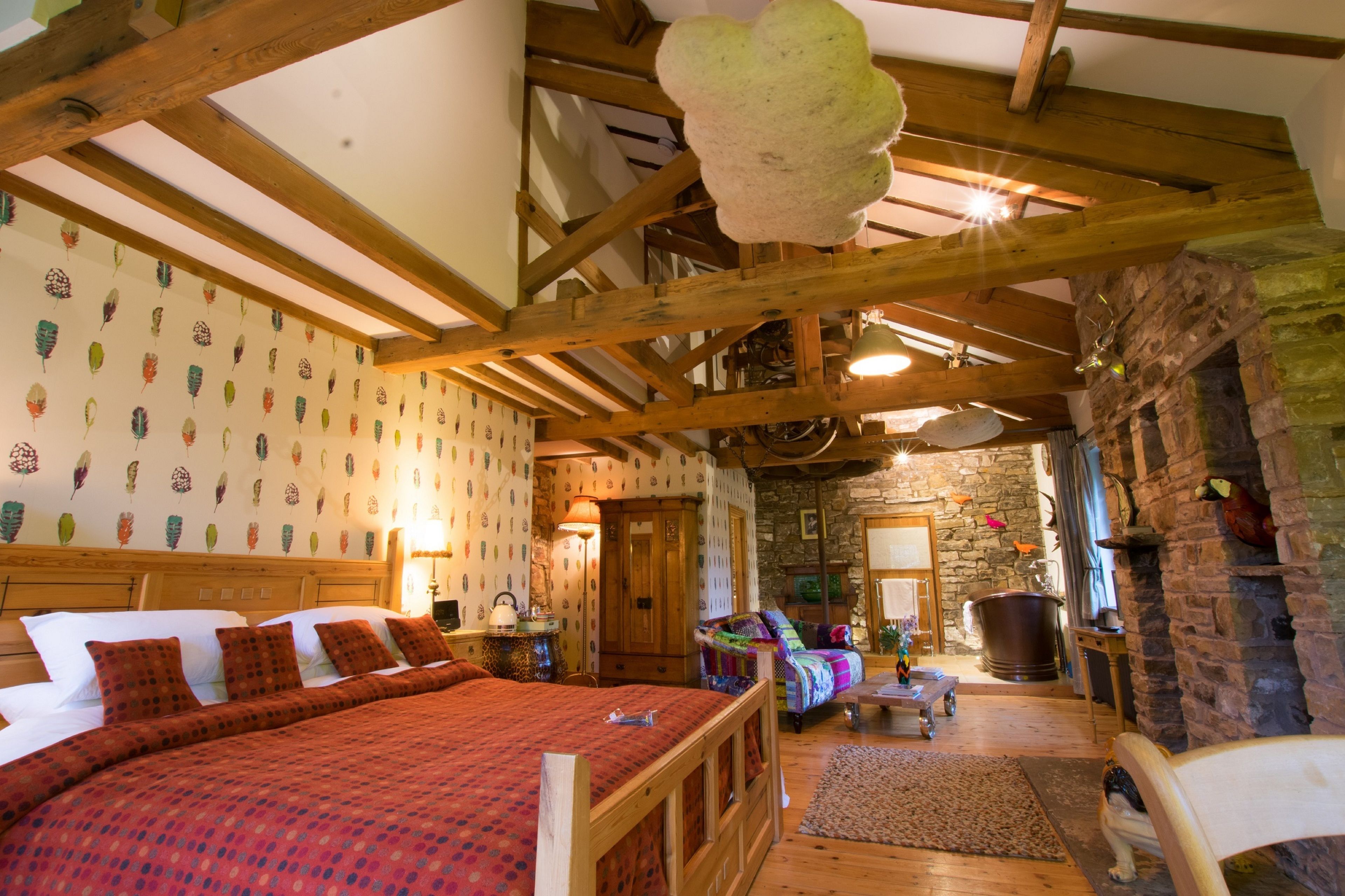 A cozy room with a wooden ceiling, a large bed with a red blanket, a stone fireplace, and a rustic decor.