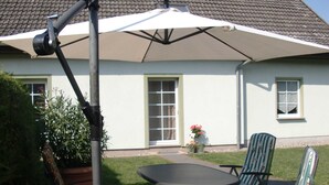 An outdoor patio with a table and chairs, a large umbrella, and a house in the background.