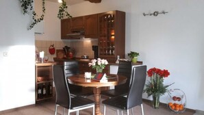 A dining area with a round table, four chairs, a vase with flowers, and a fruit bowl.