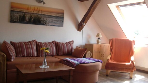 A cozy living room with a sofa, a coffee table, a chair, a painting, and a skylight.