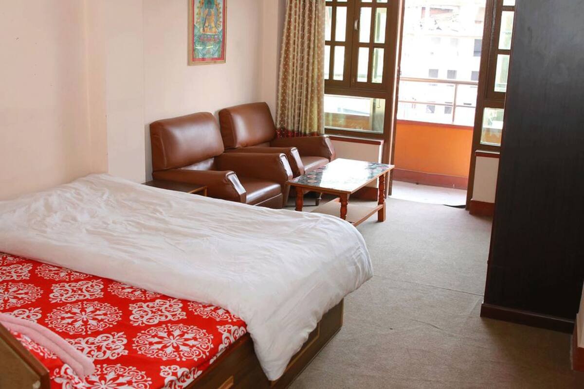 A hotel room with a bed, a sofa, a small table, and a view of the outside through a window.
