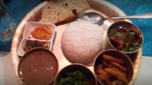 Comida tradicional india servida en un plato de cobre con arroz, dal, verduras mixtas y un trozo de pan.