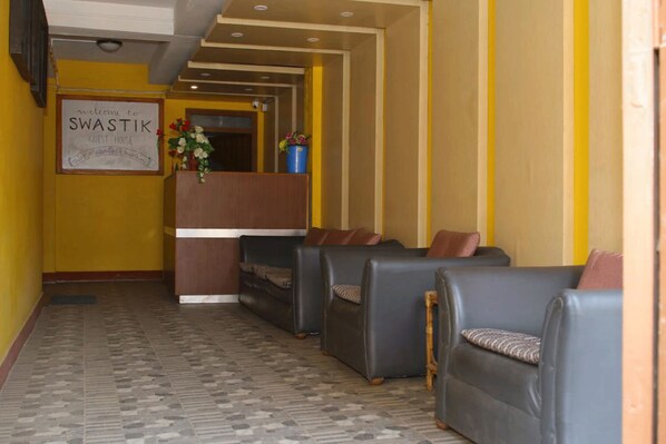 Un área de recepción con un cartel que dice “Welcome to Swastik Guest House”, un mostrador de recepción y varios sofás de cuero.