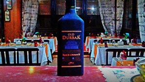 Una botella de vino Old Durbar Black Chimney sobre una mesa en un restaurante con varias mesas y sillas.