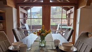 A dining table set with white cups, a glass, and a vase with yellow tulips, with a view of a wooden deck and greenery outside. - Ferienwohnung "Holunder" 55 qm bis 2 Personen, 2. Obergeschoss, 1 separates Schlafzimmer zwei Betten in Überlänge. Südbalk (Bad Feilnbach)