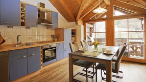 A modern kitchen with wooden beams, a dining area with a table and chairs, and large windows. - Ferienwohnung "Holunder" 55 qm bis 2 Personen, 2. Obergeschoss, 1 separates Schlafzimmer zwei Betten in Überlänge. Südbalk (Bad Feilnbach)