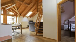 A spacious loft with high ceilings, wooden beams, a dining area, a staircase, and a cozy bedroom. - Ferienwohnung "Holunder" 55 qm bis 2 Personen, 2. Obergeschoss, 1 separates Schlafzimmer zwei Betten in Überlänge. Südbalk (Bad Feilnbach)