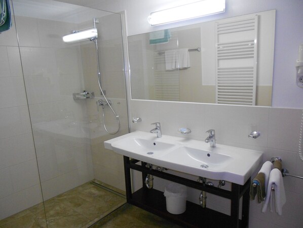 A bathroom with a glass-enclosed shower, a white sink with two basins, and a mirror above the sink. - (21) Two-room vacation apartment 50 sqm, bathroom/WC, kitchen, balcony (Reit im Winkl)